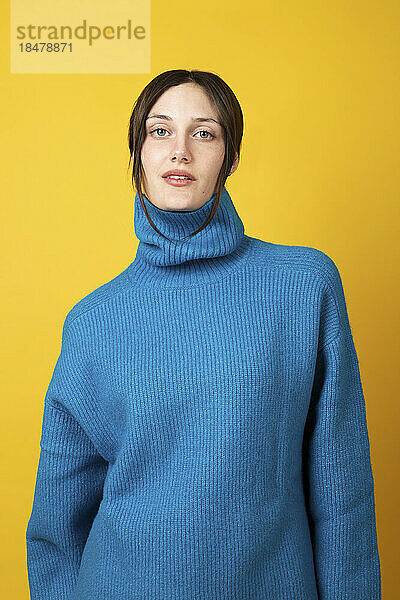 Confident young woman wearing blue turtleneck against yellow background