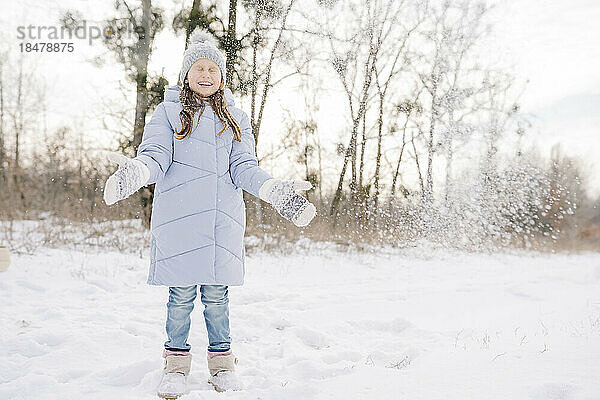 Fröhliches Mädchen mit Fäustlingen und Strickmütze spielt im Schnee