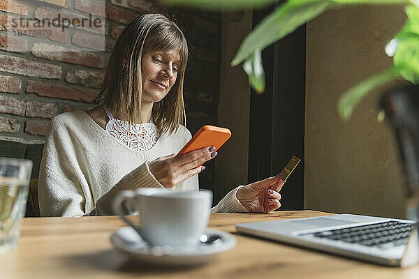 Lächelnder Freiberufler mit Kreditkarte und Smartphone im Café