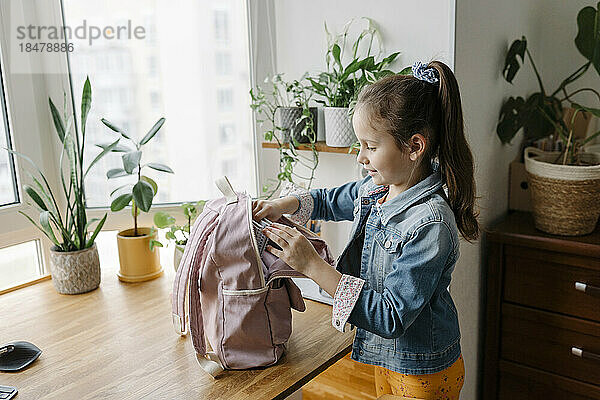 Lächelndes Mädchen  das zu Hause den Rucksack auf dem Tisch öffnet