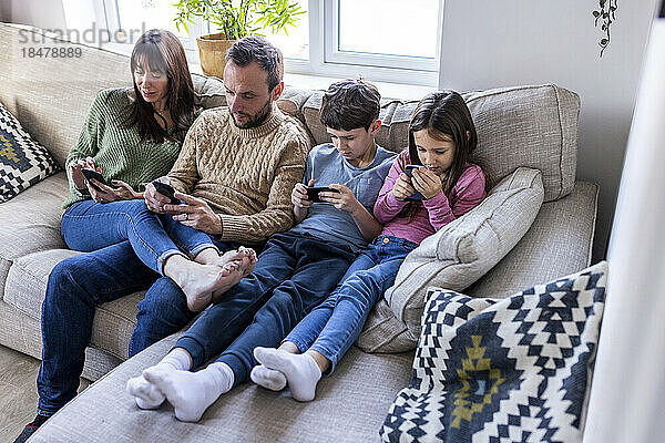 Familie benutzt Mobiltelefone auf dem Sofa im Wohnzimmer zu Hause