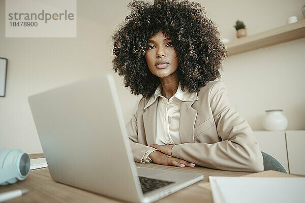 Selbstbewusste junge Geschäftsfrau mit Afro-Frisur sitzt vor Laptop