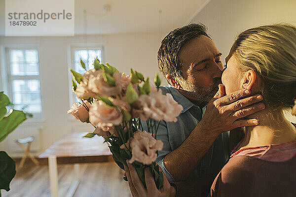 Zärtlicher Ehemann küsst Ehefrau und hält zu Hause einen Blumenstrauß