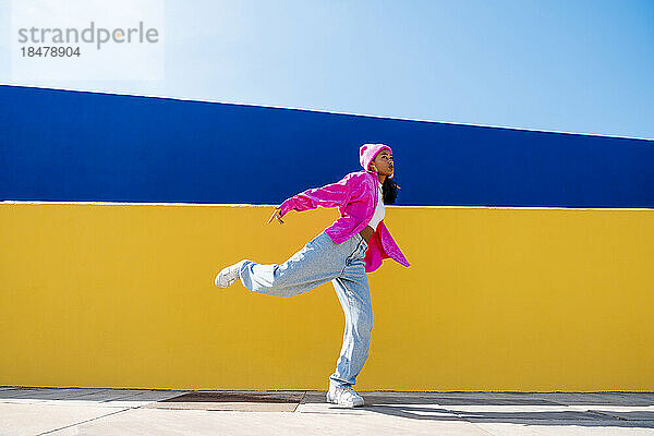 Junge Frau tanzt an einem sonnigen Tag vor einer Mauer Breakdance