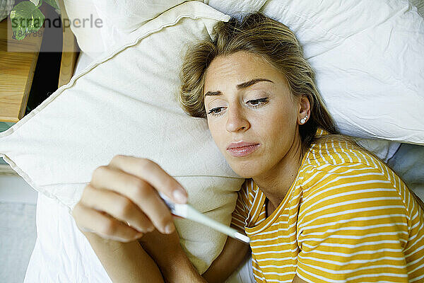 Kranke Frau überprüft zu Hause im Bett die Temperatur mit einem Thermometer