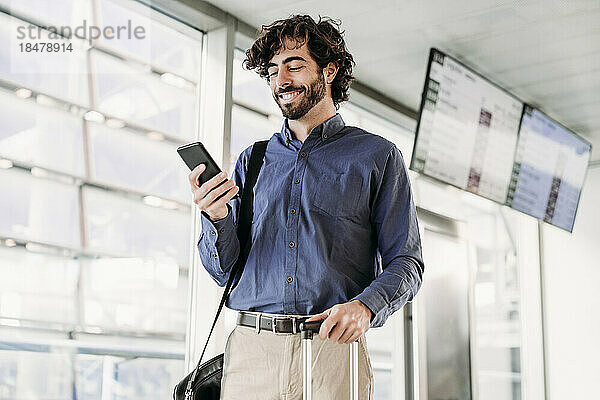Lächelnder junger Geschäftsmann  der am Bahnhof sein Mobiltelefon benutzt