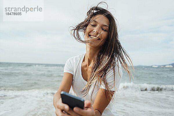 Sorglose Frau benutzt Mobiltelefon am Strand