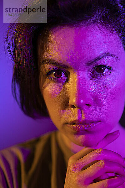 Junge Frau mit Neonbeleuchtung im Gesicht vor Hintergrund