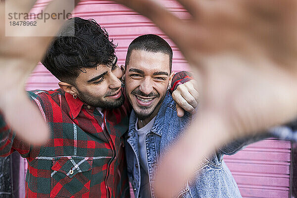 Happy gay couple gesturing in front of pink roller shutter