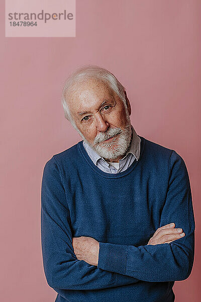 Älterer Mann mit verschränkten Armen vor rosa Hintergrund
