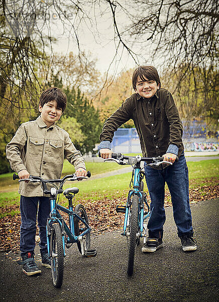 Lächelnde Brüder mit Fahrrädern stehen auf dem Fußweg im Park