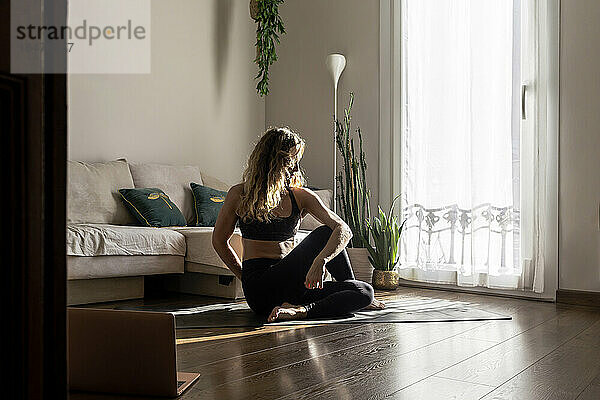 Frau praktiziert Yoga auf Matte im heimischen Wohnzimmer