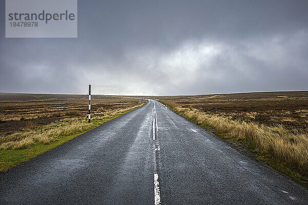 Leere Straße inmitten eines Feldes unter Gewitterwolken  County Durham  England