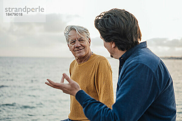 Lächelnder älterer Mann mit Sohn  der vor dem Meer diskutiert