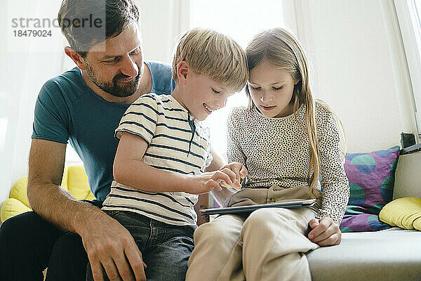 Lächelnder Sohn und Tochter teilen sich zu Hause einen Tablet-PC