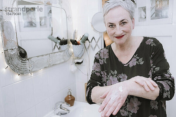Lächelnde ältere Frau  die im Badezimmer Handcreme aufträgt