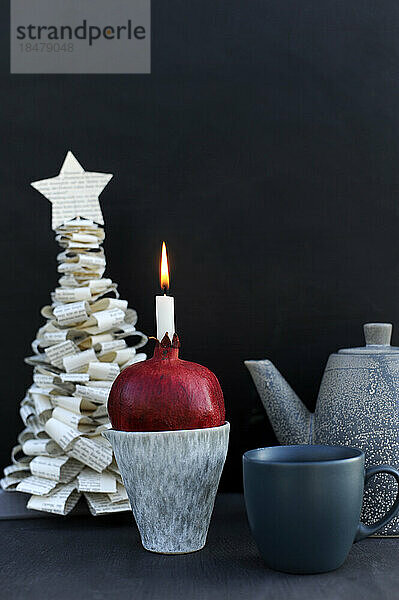 DIY-Weihnachtsbaum aus Buchseiten und brennender Kerze im Inneren eines Granatapfels