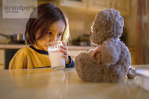 Junge blickt auf Teddybär auf dem Tisch und trinkt Milch