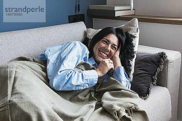 Lächelnde Frau entspannt sich auf dem Sofa im Wohnzimmer
