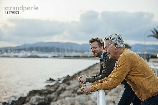 Glücklicher Vater und Sohn lehnen sich am Geländer vor dem Meer
