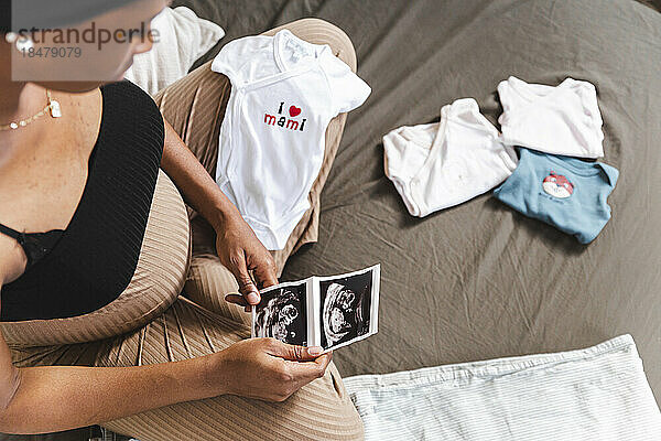 Pregnant woman holding ultrasound scan on bed at home