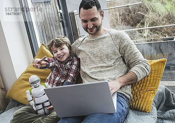 Glücklicher Sohn zeigt Friedenszeichen  während Vater zu Hause Laptop benutzt