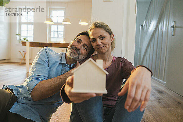 Lächelndes Paar blickt auf das Hausmodell  das zu Hause sitzt