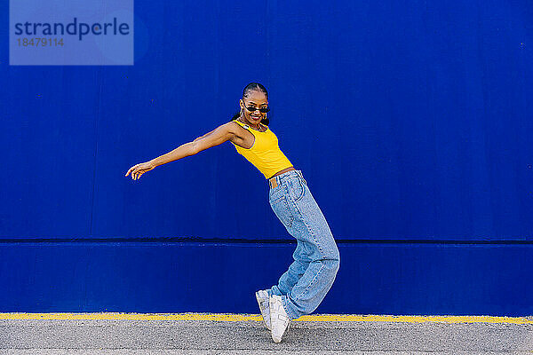 Tänzerin tanzt auf Zehenspitzen an der blauen Wand auf dem Fußweg