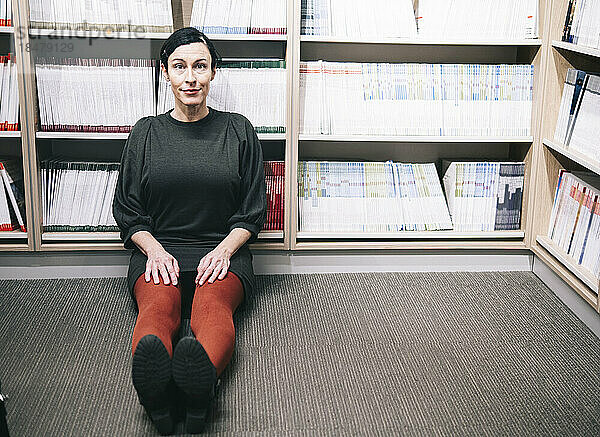 Lächelnde Frau sitzt vor Bücherregal in der Bibliothek