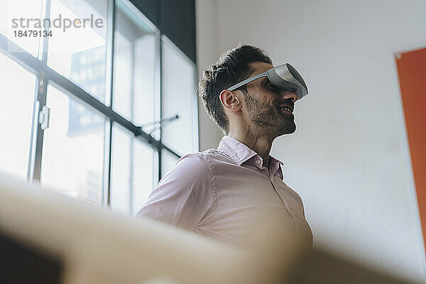 Lächelnder reifer Geschäftsmann mit VR-Brille im Büro