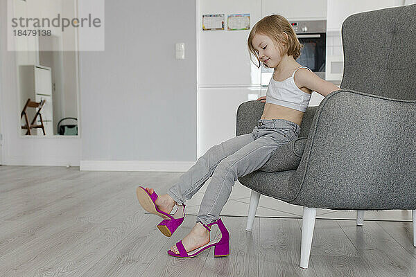 Girl wearing mother's shoes sitting on chair at home