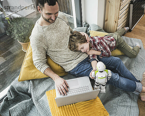 Sohn schläft  während Vater zu Hause Laptop benutzt