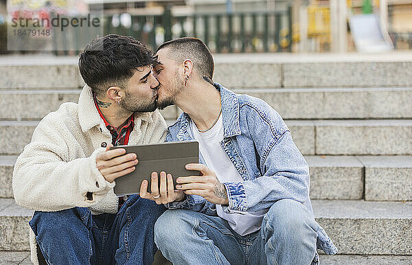 Romantisches schwules Paar küsst sich mit Tablet-PC auf Stufen