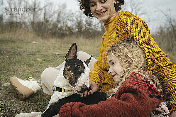 Glückliche Mutter und Mädchen sitzen mit Bullterrier-Hund