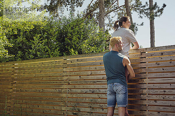 Glücklicher Mann mit Frau blickt über Holzzaun im Hinterhof