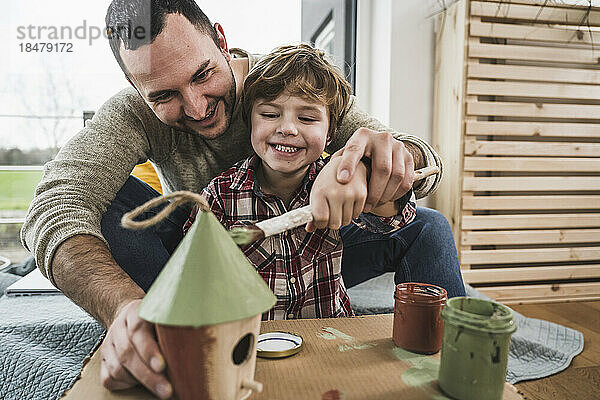 Glücklicher Vater und Sohn malen zu Hause gemeinsam ein Musterhaus