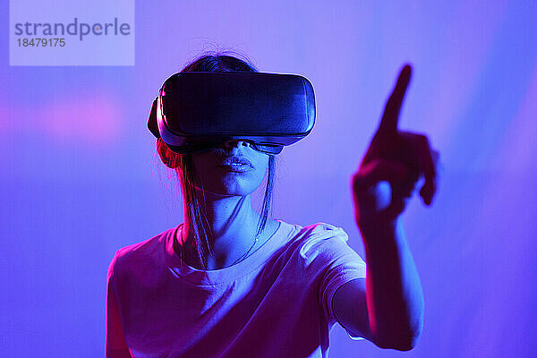Frau mit VR-Brille zeigt auf farbigen Hintergrund