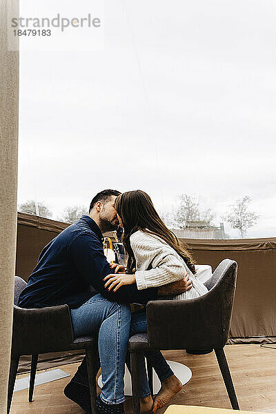 Young couple sitting on chair kissing in dome tent hotel