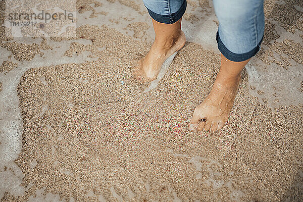 Frau steht auf nassem Sand am Strand