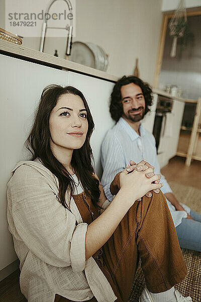 Thoughtful woman sitting with boyfriend in kitchen at home