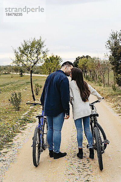 Young couple with bicycles kissing on dirt road