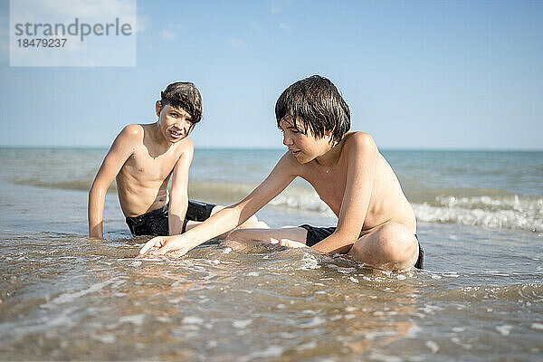Brüder spielen zusammen und sitzen im nassen Sand am Ufer des Strandes