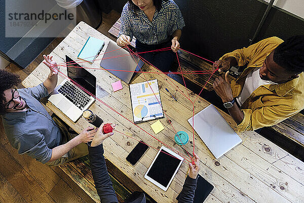 Business colleagues playing cat's cradle sitting at desk in office