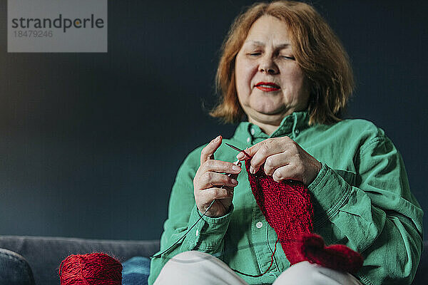 Ältere Frau strickt zu Hause roten Pullover mit Nadel