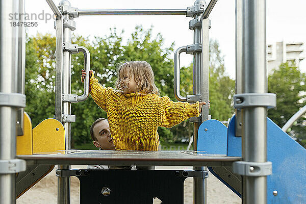 Vater hilft Tochter beim Erklimmen der Rutsche auf dem Spielplatz