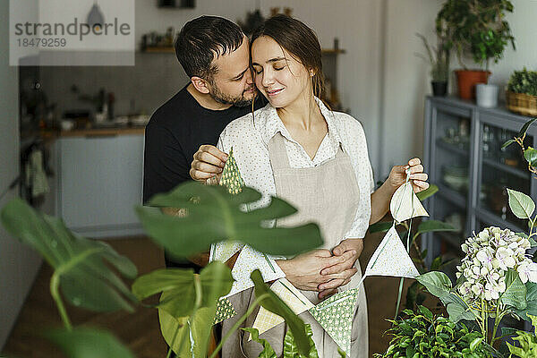 Liebevolles Paar mit Girlanden aus frischen Pflanzen zu Hause