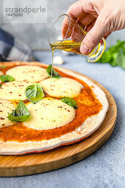 Hand einer Frau gießt Öl auf Pizza