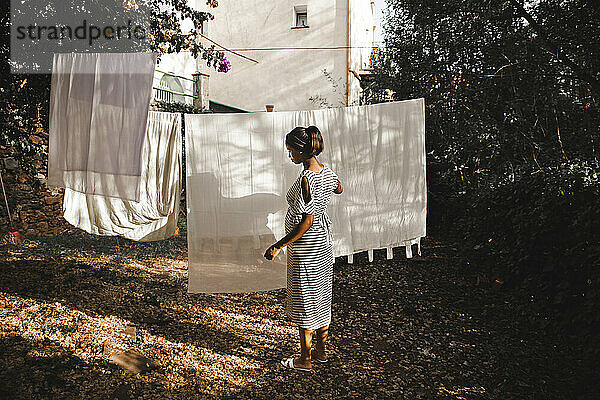 Schwangere Frau hängt weißes Laken im Hinterhof im Garten auf