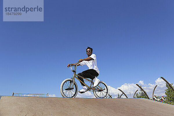 Mann sitzt an einem sonnigen Tag auf einem BMX-Fahrrad unter dem Himmel