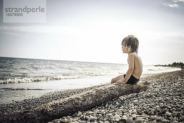 Shirtless boy sitting on log at beach